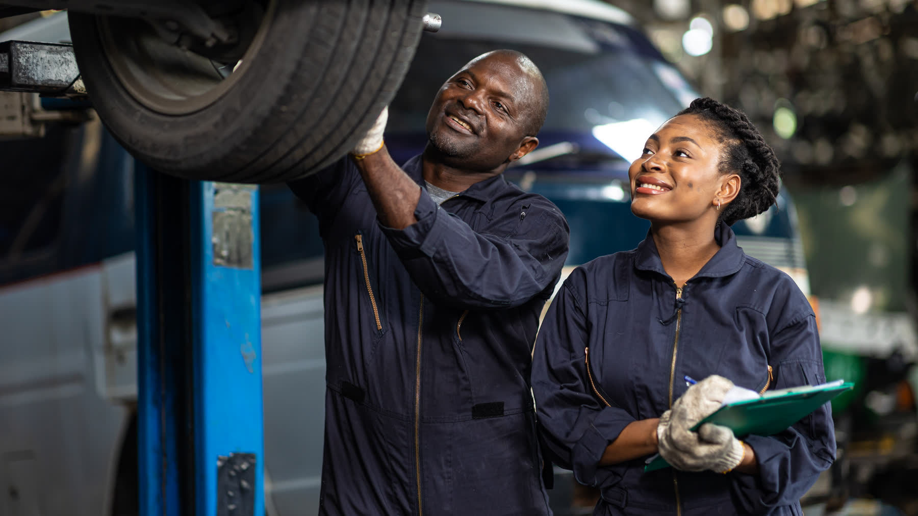 Two workshop technicians in overalls inspecting a vehicle on a lift